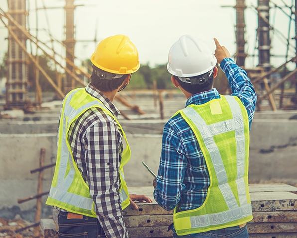 Two contractors looking at a construction site. The one on the right is pointing at a detail in the build.